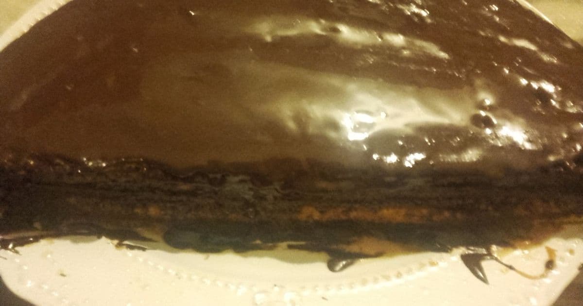 Un bizcocho de chocolate con un generoso glaseado de dulce de leche y un poco de cacao en polvo espolvoreado, cortado en porciones sobre un plato de cerámica rústica.