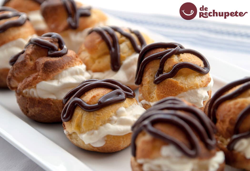 Profiteroles de nata y chocolate con glaseado brillante, presentados elegantemente en un plato de cerámica blanca.
