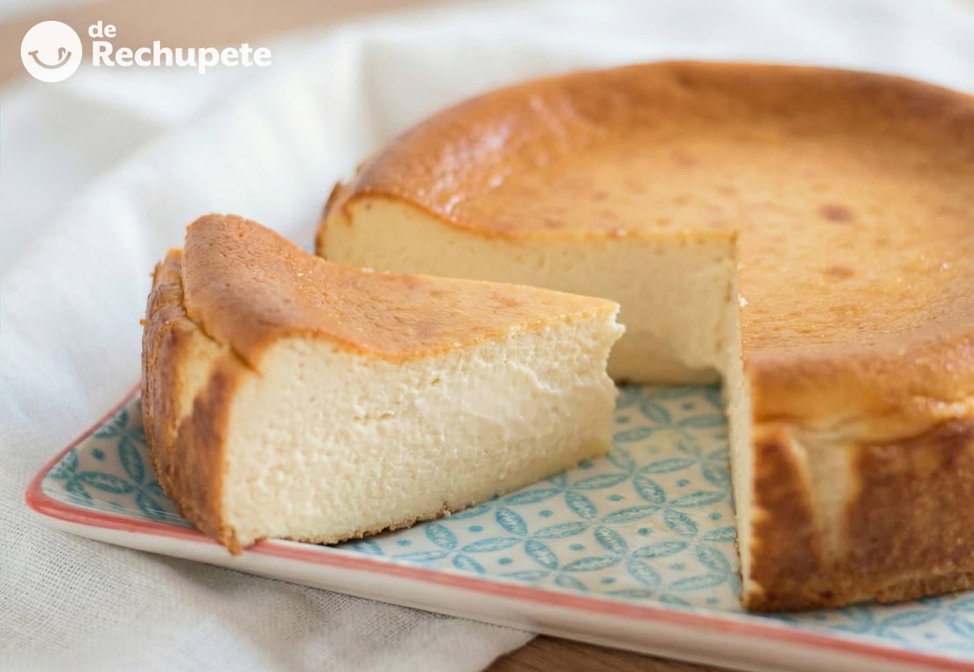 Tarta de queso al horno recién salida del horno, superficie dorada y corteza ligera, reposando sobre un plato de cerámica blanca